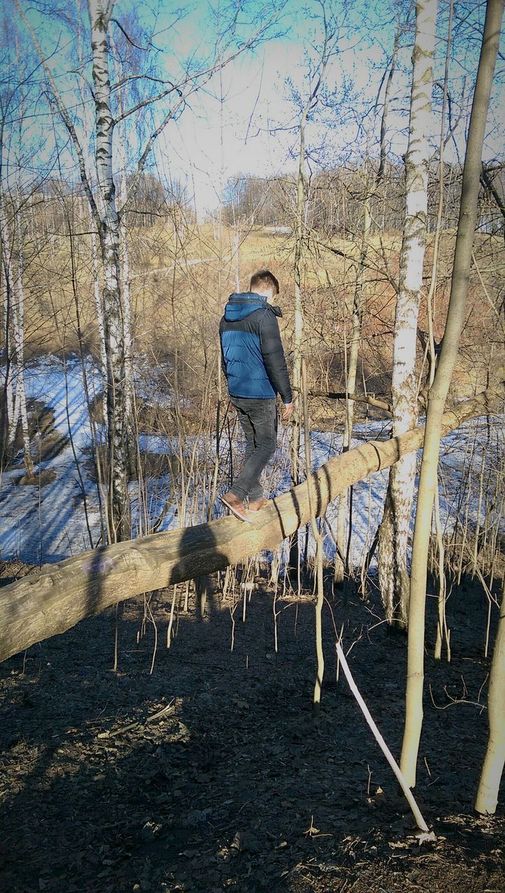 tree, day, lifestyles, leisure activity, blue, water, relaxation, bare tree, rear view, outdoors, standing, built structure, nature, wood - material, sunlight, full length, abandoned, tranquility