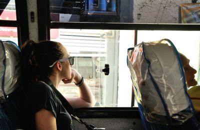 Woman looking though window while sitting in bus