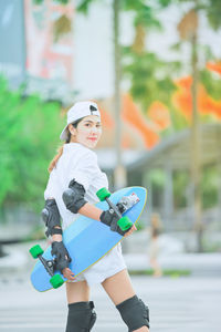 Portrait of woman holding skateboard while standing outdoors
