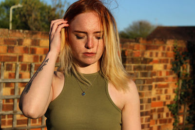 Portrait of young woman standing against brick wall