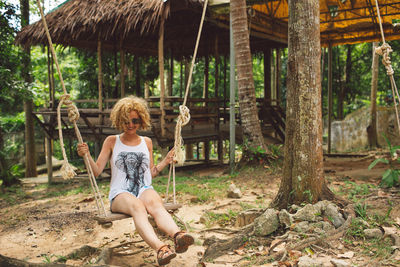 Full length of woman sitting on swing in forest