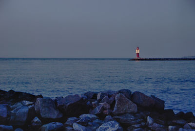 Lighthouse by sea against clear sky during sunset