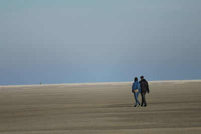 Rear view of man and woman walking on sand