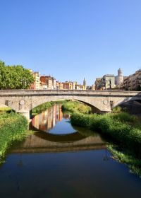 Arch bridge over river by buildings against clear blue sky