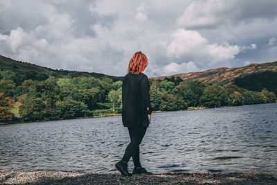 Young woman standing by lake against cloudy sky