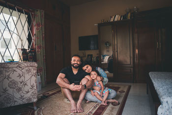 Portrait of smiling parents sitting with daughter on carpet in living room at home