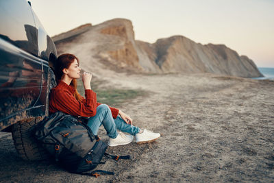 Young woman sitting on rock against sky