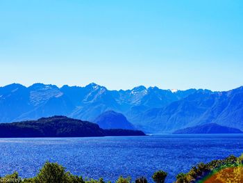 Scenic view of lake and mountains against clear blue sky