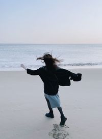 Rear view of woman standing at beach against sky