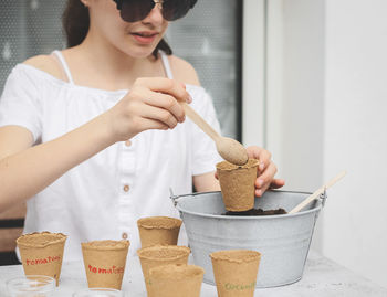 Caucasian teenage girl picks up soil from a zinc bucket for a cardboard cup with a wooden spoon