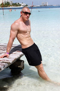 Portrait of shirtless man leaning on jetty at beach