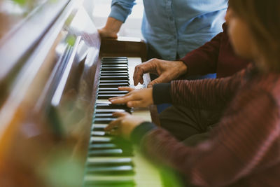 Midsection of woman standing by boy and great grandfather playing piano