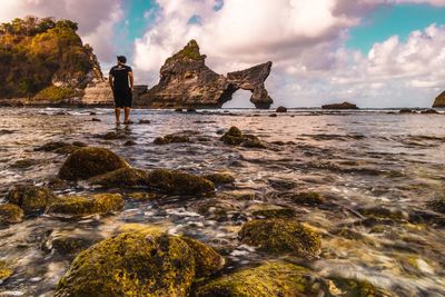 Rear view of man standing at beach against cloudy sky