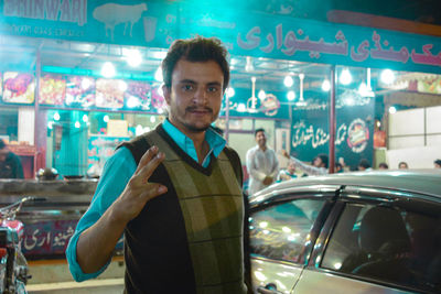 Portrait of man showing peace sign against restaurant at night