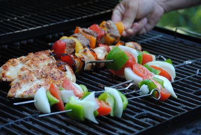 Cropped hand holding skewers on barbecue grill