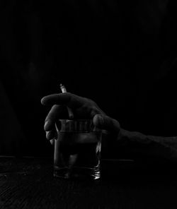 Cropped hand holding cigarette and drink on table against black background