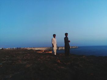 Friends standing on sea shore against clear sky