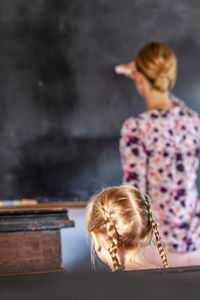 Rear view of teacher teaching female student in classroom