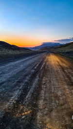 Dirt road passing through landscape against sky during sunset