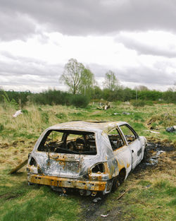 Abandoned car on field against sky