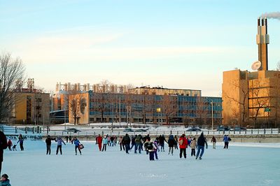 People skating at rideau canal skateway against sky in city