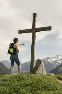 Woman pointing at cross on mountain peak