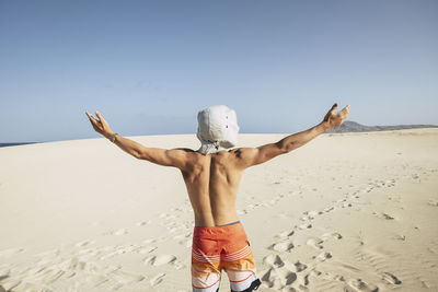 Rear view of shirtless man standing on beach against clear sky