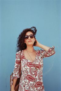 Portrait of young woman wearing sunglasses standing against wall