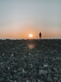 Man standing on rock against sky during sunset