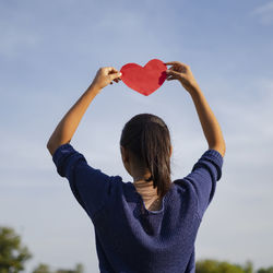 Midsection of woman holding heart shape against sky