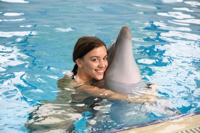 Portrait of smiling young woman with dolphin swimming in pool