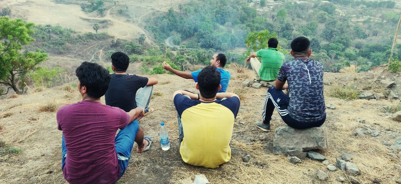 REAR VIEW OF PEOPLE SITTING ON MOUNTAIN