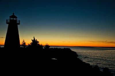 Silhouette lighthouse by sea against sky during sunset