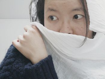 Close-up of mid adult woman covering face with white scarf at home