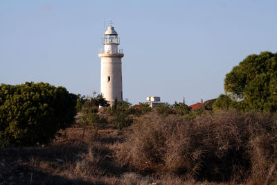 Lighthouse amidst trees and buildings against sky