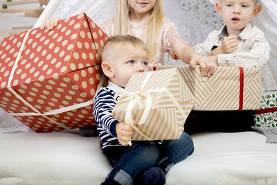 Three children kids holding christmas gift boxes in a decorated house.
