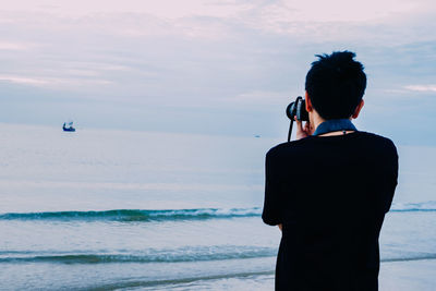 Rear view of man photographing against sea and sky