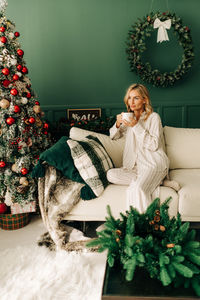 European woman sitting in pajamas in the living room on christmas eve drinking hot cocoa.
