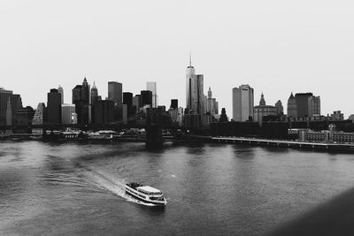 Boats in river by cityscape against clear sky