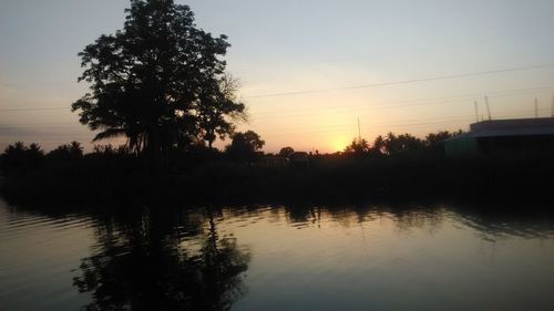 Silhouette trees by lake against clear sky during sunset