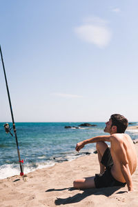 Man sitting at beach against sky