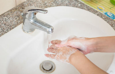 Cropped image of person washing hands at bathroom sink