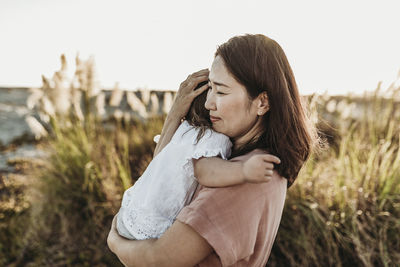 Mid view of loving mom embracing young daughter at beach during sunset