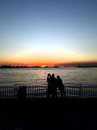 Silhouette people on beach against clear sky during sunset