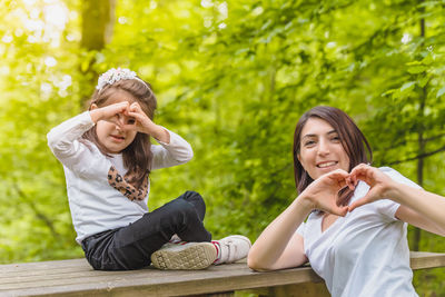 Smiling young woman sitting on plant against trees