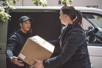 Side view of delivery woman giving package to coworker outside truck