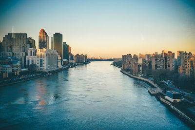 Scenic view of river amidst buildings in city during sunset