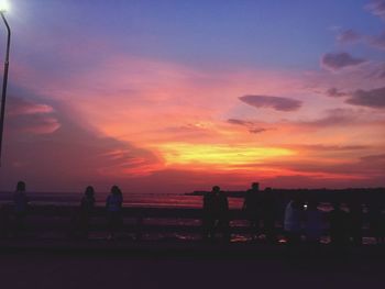 Silhouette people standing by sea against sky during sunset