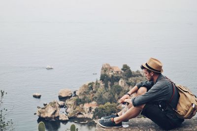 Young man sitting on rock by sea