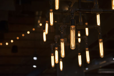 Close-up of illuminated light bulb hanging outdoors at night